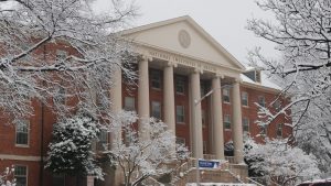 Snow-covered trees frame the red-brick National Institutes of Health building with white columns and a 'James A. Shannon Building' sign