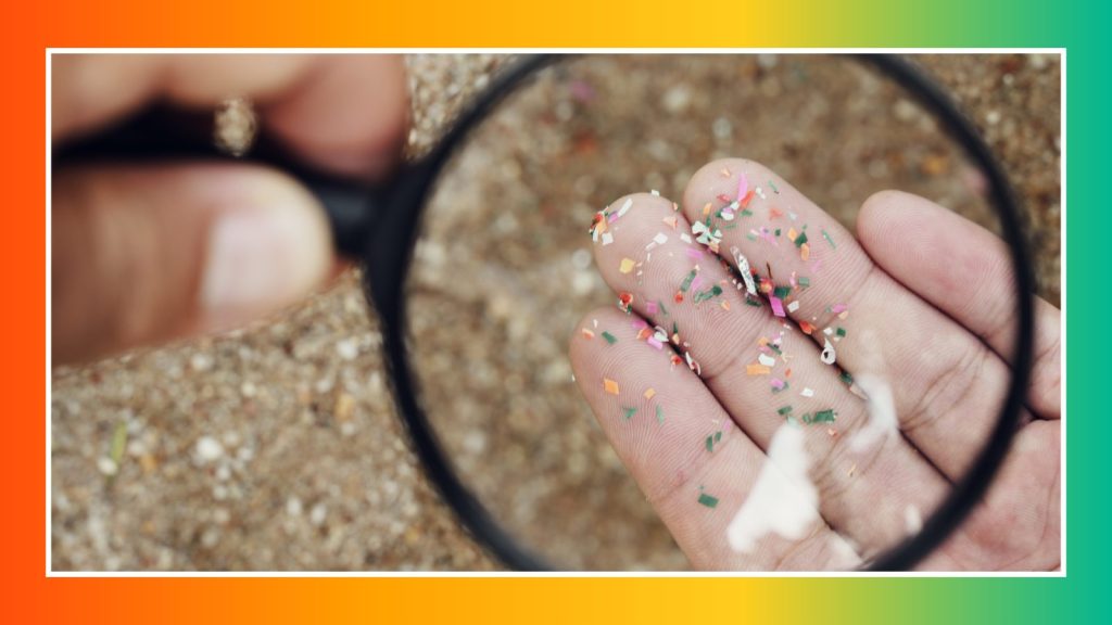 Hand holding up microplastics to a magnifying glass